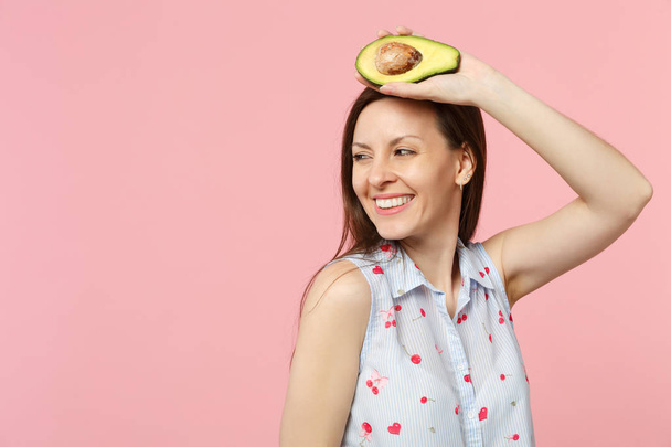 Smiling young woman in summer clothes looking aside holding fresh ripe green avocado fruit isolated on pink pastel wall background. People vivid lifestyle relax vacation concept. Mock up copy space. - Fotografie, Obrázek