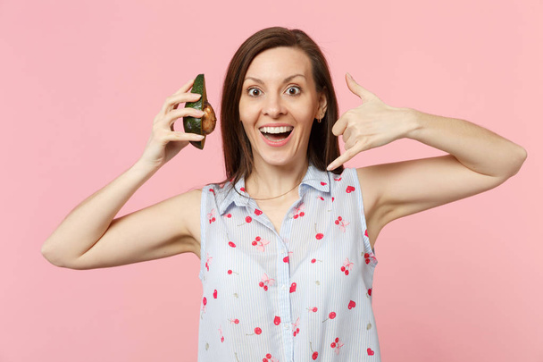 Excited woman doing phone gesture like says call me back holding half of fresh ripe avocado fruit isolated on pink pastel background. People vivid lifestyle relax vacation concept. Mock up copy space. - Photo, Image