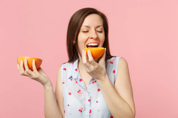 Cheerful young woman keeping eyes closed hold, biting halfs of fresh ripe grapefruit orange fruit isolated on pink pastel background. People vivid lifestyle relax vacation concept. Mock up copy space. - Fotó, kép