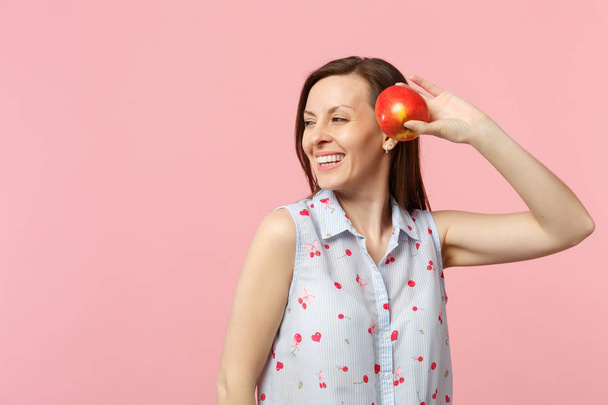 Jovem sorridente em roupas de verão olhando para o lado segurando fruta fresca de maçã vermelha madura isolada em fundo pastel rosa no estúdio. Pessoas estilo de vida vívido, relaxar conceito de férias. Mock up espaço de cópia
. - Foto, Imagem