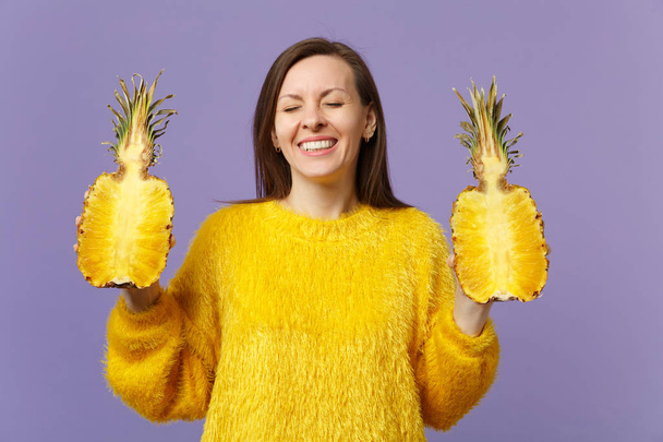Usmívající se mladá žena v kožešinových svetru, která drží oči zavřené, drží na fialovém pozadí halfs čerstvě zralých ananasových plodů. Lidé živý životní styl relaxace dovolené. Vysmívat prostor pro kopírování. - Fotografie, Obrázek