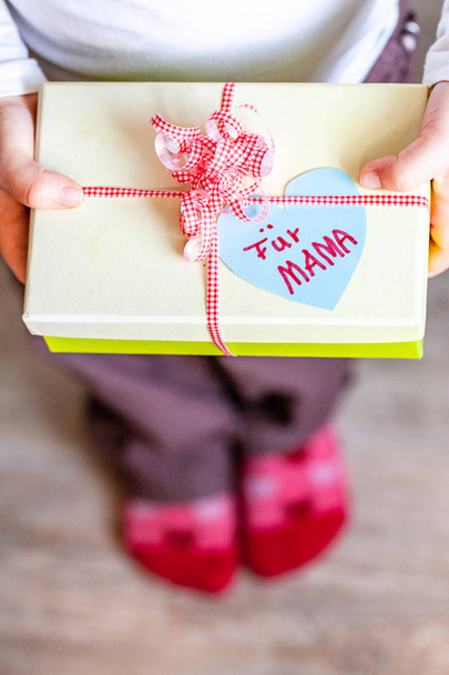 Little child holding gift box with ribbon and heart for her mum - Translation: for mum - Foto, Bild