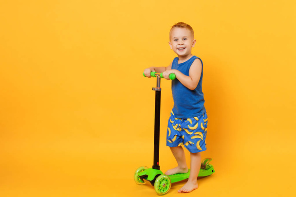 Kid boy 3-4 years old wearing blue beach summer clothes on scoot - Photo, image