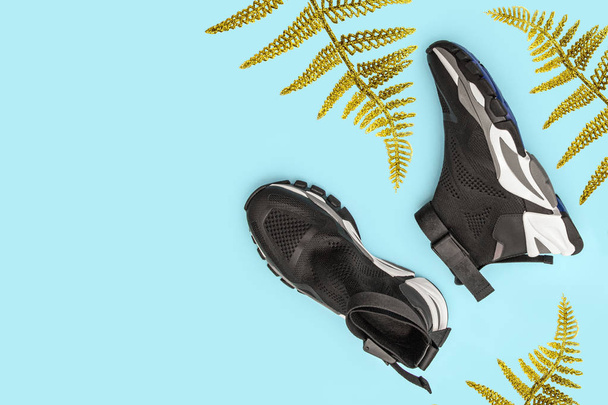 Woman fashion black sport shoes with gold fern leaf, palm frond on blue background. Top view, copy space. - Фото, изображение