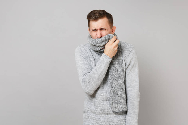 Ailing young man in gray sweater covering mouth with scarf sneez - Photo, Image
