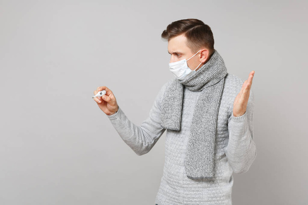 Fiatal férfi pulóvert, sálat steril álarc nézi hőmérő - Fotó, kép