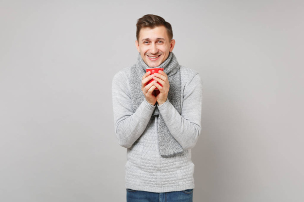 fröhlicher junger Mann in grauem Pullover, Schal mit rotem Kaffeebecher - Foto, Bild