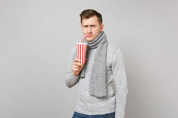 Hombre joven preocupado en suéter gris bufanda beber cola o refresco
  - Foto, Imagen