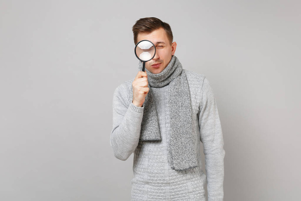 junger Mann im grauen Pullover, Schal in der Hand, Blick unter die Lupe - Foto, Bild