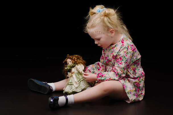 A little girl plays with a doll on a black background. - Fotoğraf, Görsel