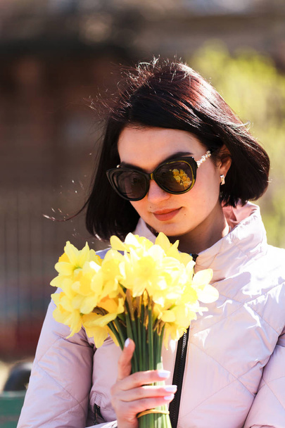 Bir buket Daffodils tutan güneş gözlüğü genç güzel esmer kız. Bir avuç çiçek - Fotoğraf, Görsel