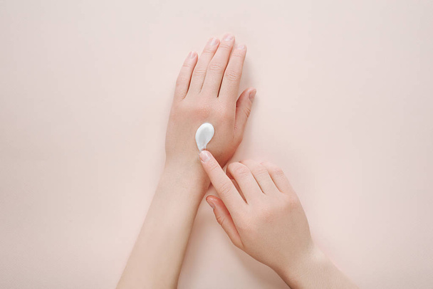 Woman moisturizing her hand with cosmetic cream lotion with copy space on beige background. Concept template feminine blog, beauty concept - Fotó, kép