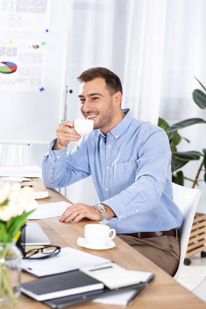 cheerful businessman holding cup of coffee while sitting in office - Fotoğraf, Görsel