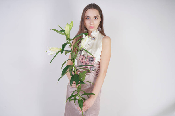 bájos fiatal kaukázusi lány egy szép ruhát tart a buja liliom virágot a kezében, és áll a fehér háttér a stúdióban egyedül - Fotó, kép