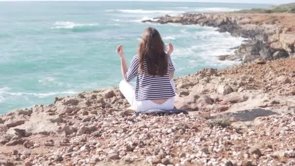 Молода жінка сидить у позі лотоса на скелі біля моря
. - Кадри, відео