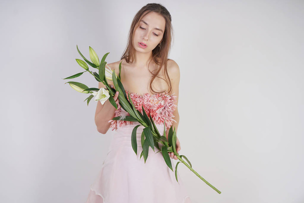 encantadora chica caucásica joven en un bonito vestido tiene una exuberante flor de lirio en sus manos y se encuentra sobre un fondo blanco en el estudio solo
 - Foto, imagen