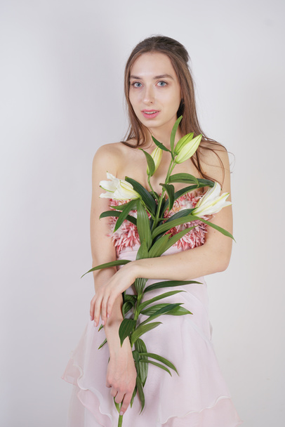 charming young caucasian girl in a pretty dress holds a lush Lily flower in her hands and stands on a white background in the Studio alone - Foto, Imagen