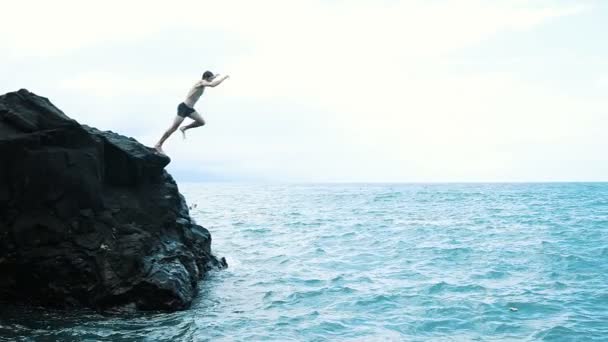 Młody człowiek skaczący z urwiska do błękitnego morza. Aktywny i przyjemny urlop letni. - Materiał filmowy, wideo