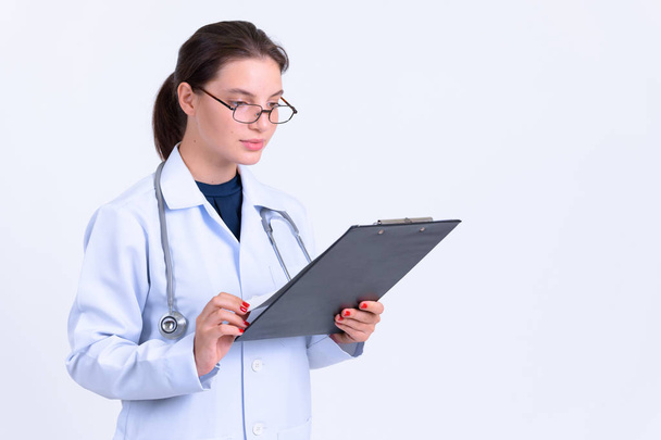 Portrait of young beautiful woman doctor reading on clipboard - Photo, image