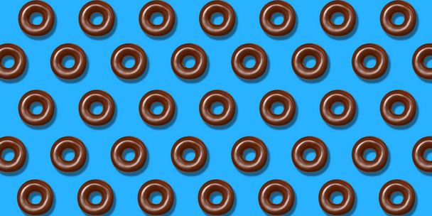 Patrón creativo rosquillas de chocolate plano yacen sobre fondo azul pastel. Concepto mínimo de comida dulce. Surrealista pastel de rosquillas marrones vista superior para panadería. Postre de rosquilla de verano abstracto
 - Foto, Imagen