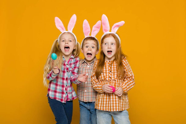 two little girls and boy with Easter bunny ears holding colorful eggs - Photo, image