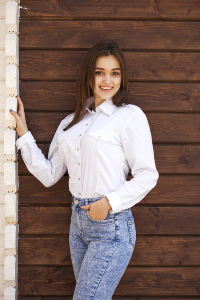 Happy teenager girl in a white shirt on a wooden wall background - Foto, Imagen