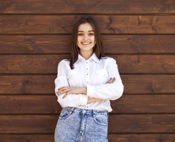 Happy teenager girl in a white shirt on a wooden wall background - Fotoğraf, Görsel