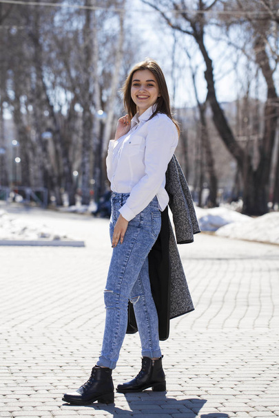 Teen girl in white shirt and blue jeans walks in spring park - Фото, изображение