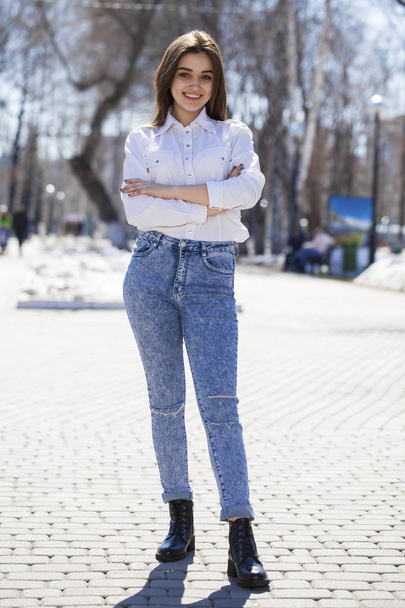 Teen girl in white shirt and blue jeans walks in spring park - Foto, afbeelding