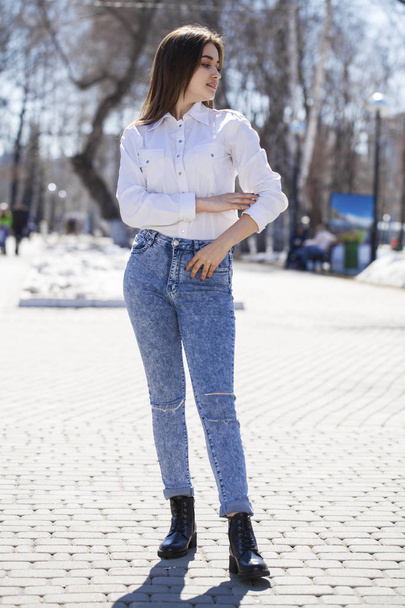 Teen girl in white shirt and blue jeans walks in spring park - Photo, image