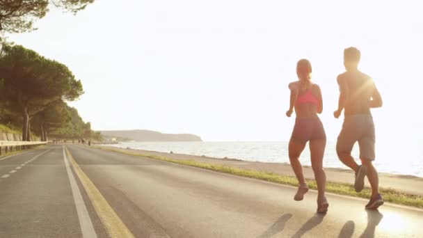 SLOW MOTION, LENS FLARE, COPY SPACE: Unrecognizable jogging couple on holiday soaking up the sun rays. Healthy couple running down beautiful sunny road overlooking the ocean. Relaxing evening jog. - Footage, Video