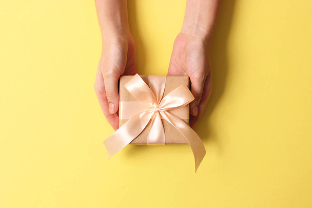 Geschenk in weiblichen Händen auf farbigem Hintergrund mit Konfetti von oben. - Foto, Bild