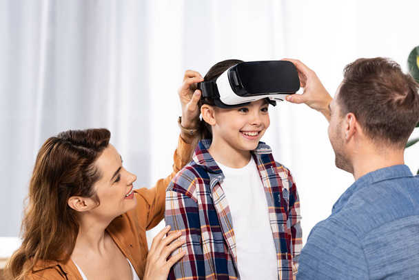 cheerful parents looking at happy kid in virtual reality headset  - Фото, зображення
