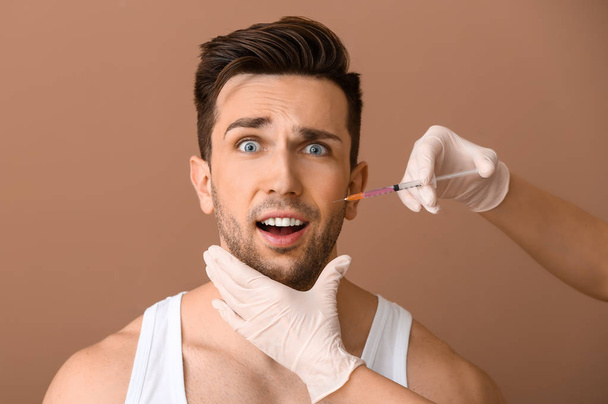 Homem assustado e mão segurando seringa para injeção anti-envelhecimento em fundo de cor
 - Foto, Imagem