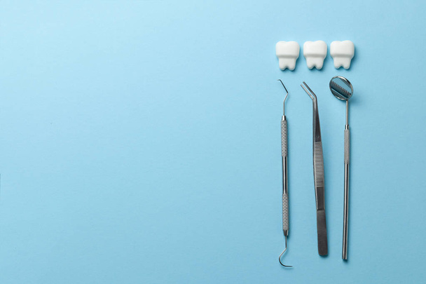 Healthy white teeth on blue background and dentist tools mirror, hook. Copy space for text. - Foto, afbeelding