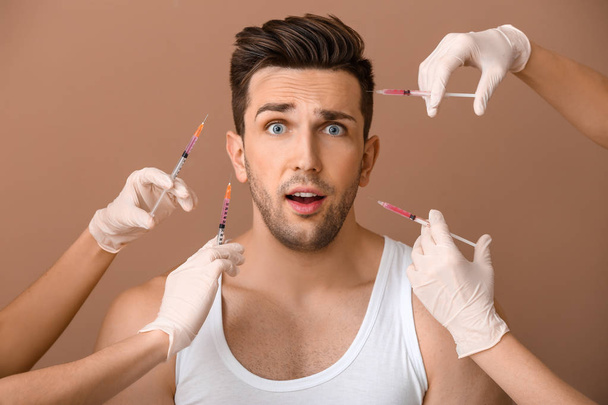 ängstlicher Mann und Hände, die Spritzen für Anti-Aging-Injektionen auf farbigem Hintergrund halten - Foto, Bild