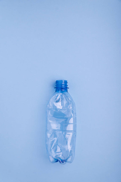 Crashed plastic bottle on bright blue background. Plastic utilisation concept. Ecological problem, global environment. - Фото, изображение