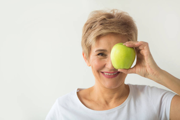 beautiful aged woman with short haircut in a white t-shirt with an apple on a white background - Photo, Image