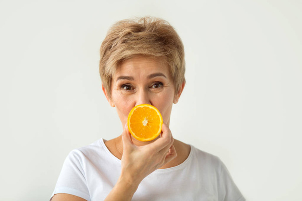 beautiful aged woman with a short haircut in a white T-shirt with oranges in her hands on a white background - Фото, зображення