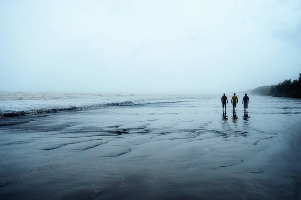 Трое мужчин, идущих в одиночестве по пляжу
. - Фото, изображение