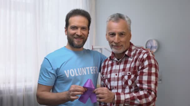 Volunteer and senior male showing purple ribbon, Alzheimer disease awareness - Footage, Video