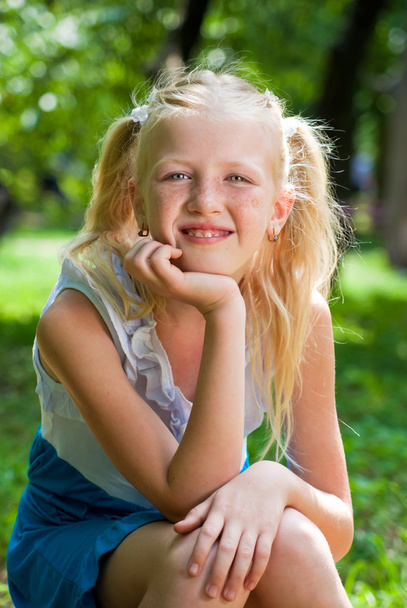 süße, verspielte blonde Mädchen sitzt im grünen Garten und Rücken - Foto, Bild