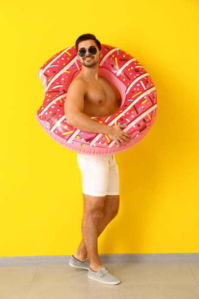 Handsome man with inflatable ring near color wall - Photo, Image