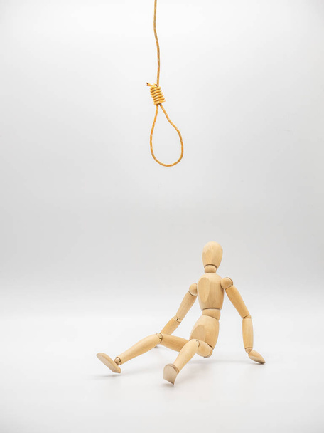 Miniature wooden doll sits under hanging rope and touch gallow noose isolated on white. Concept for thinking in crisis. - Foto, Bild