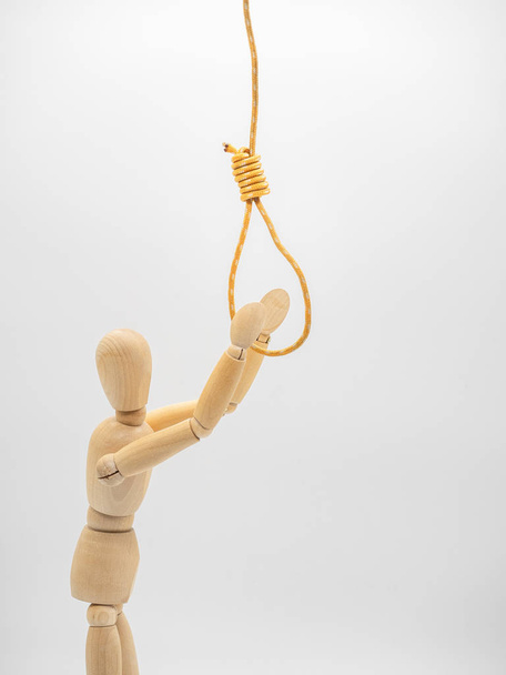 Miniature wooden doll is pulling hands to hanging rope and touch gallow noose isolated on white. Close up view.  - Fotó, kép