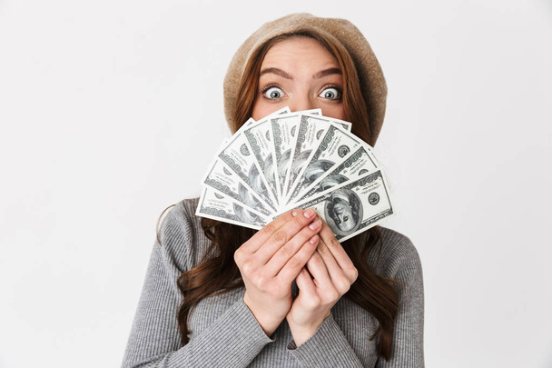 Shocked beautiful woman holding money isolated over white wall background. - Foto, afbeelding