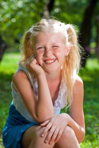 Sweet, playful blond girl sitting in the green garden and backin - Fotoğraf, Görsel