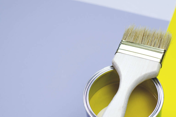 Uma lata de tinta amarela com uma escova em um cinza-amarelo com um fundo branco
. - Foto, Imagem