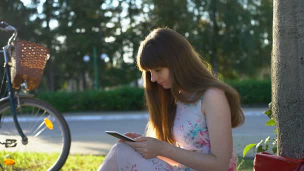 Young romantic woman sitting in park, reading e-book, smiling to herself. Summer - 映像、動画