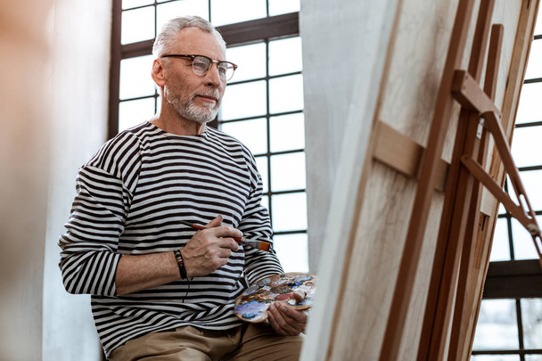 Bearded artist holding painting brush while looking on canvas - Φωτογραφία, εικόνα